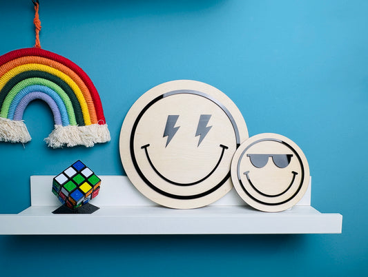 Two smiley face coasters with lightning bolt and sunglasses designs on a shelf against a blue wall.