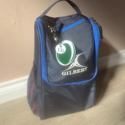 Black shoe bag with blue trim and Gilbert logo on a beige floor.