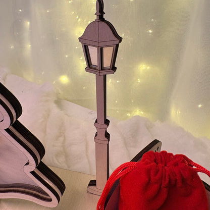 Decorative lamp post with a red bag on a light-coloured wooden surface 
