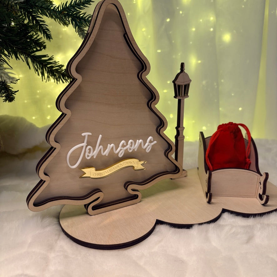 Wooden Christmas tree decoration with 'Johnsons' and a red bag on a snowy background