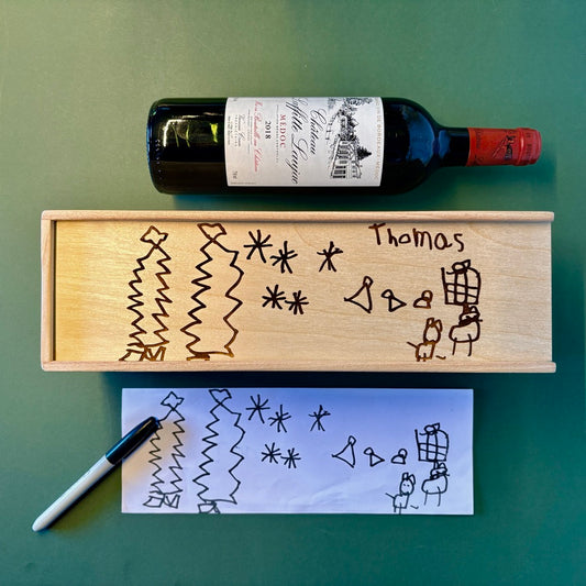 Wooden box with engraved designs and a bottle of wine on a green surface