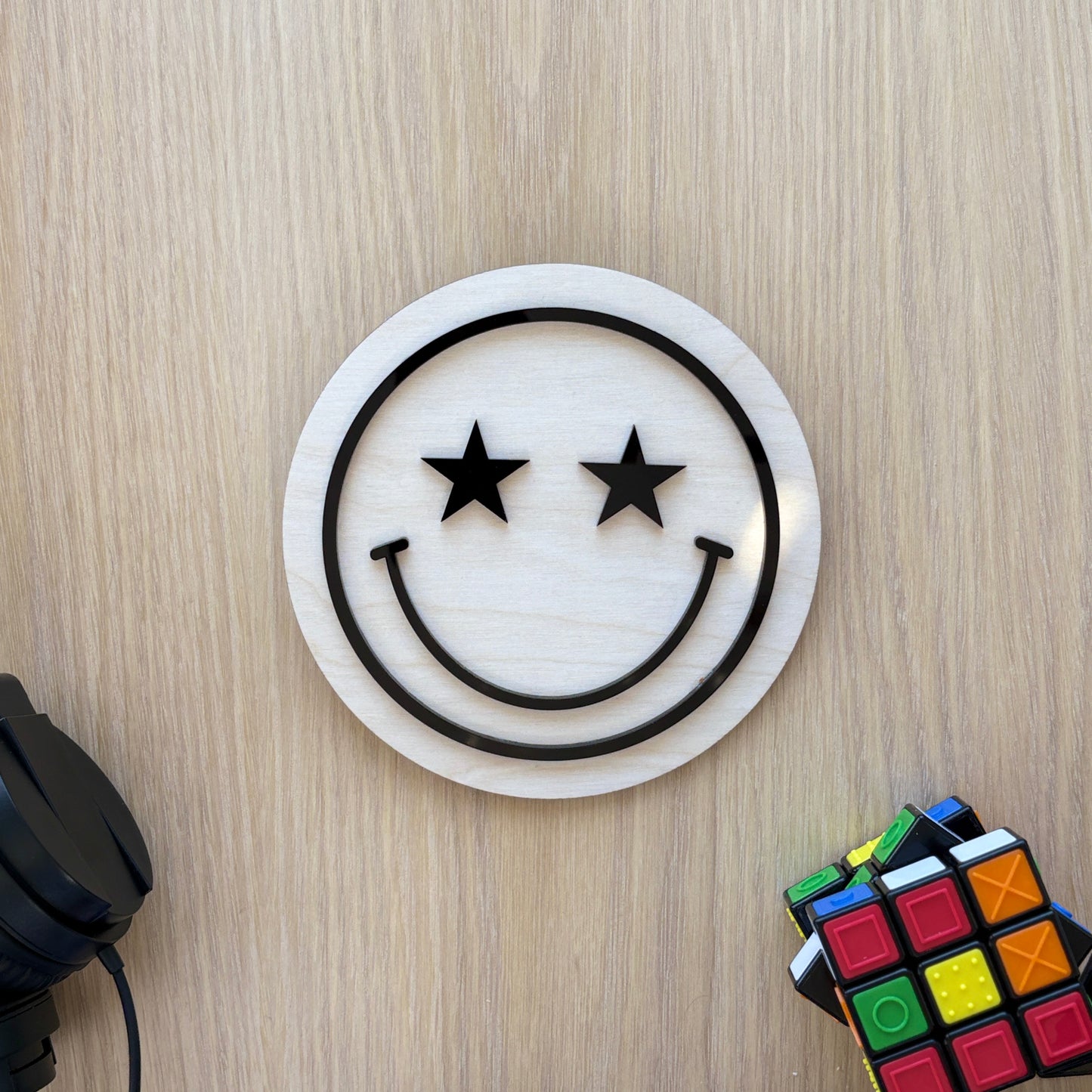 Circular object with smiley face design on a wooden surface with headphones and Rubik's cube.