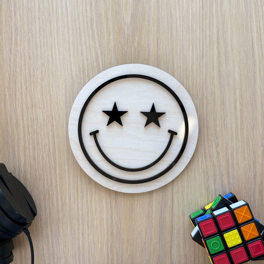 Circular object with smiley face design on a wooden surface with headphones and Rubik's cube.