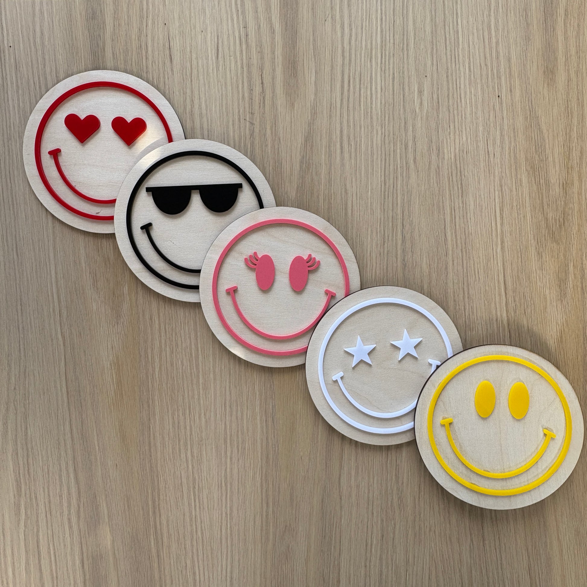 Five smiley face coasters with different designs on a wooden surface