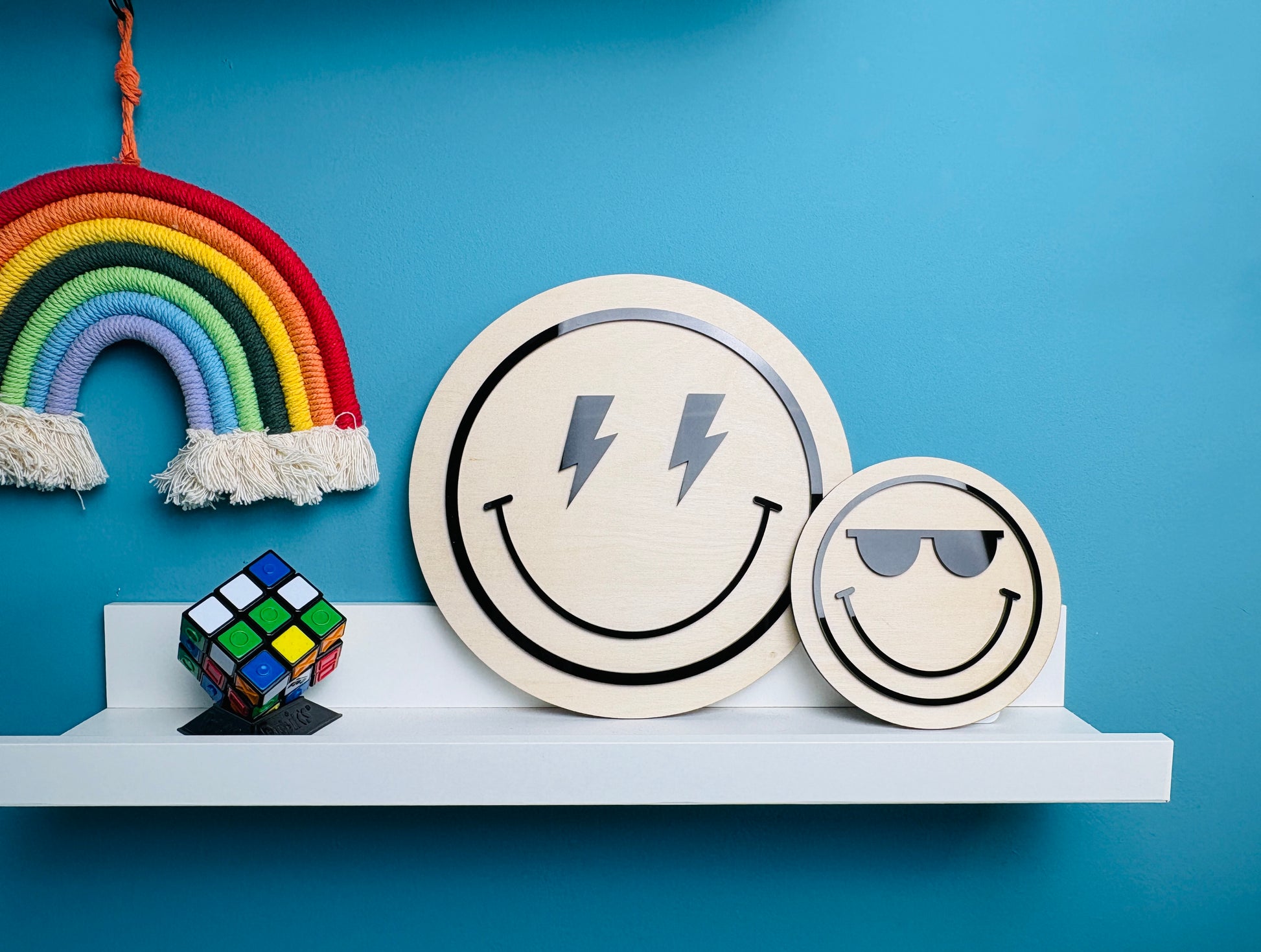 Two smiley face coasters with lightning bolt and sunglasses designs on a shelf against a blue wall.