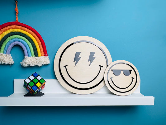 Two smiley face coasters with lightning bolt and sunglasses designs on a shelf against a blue wall.