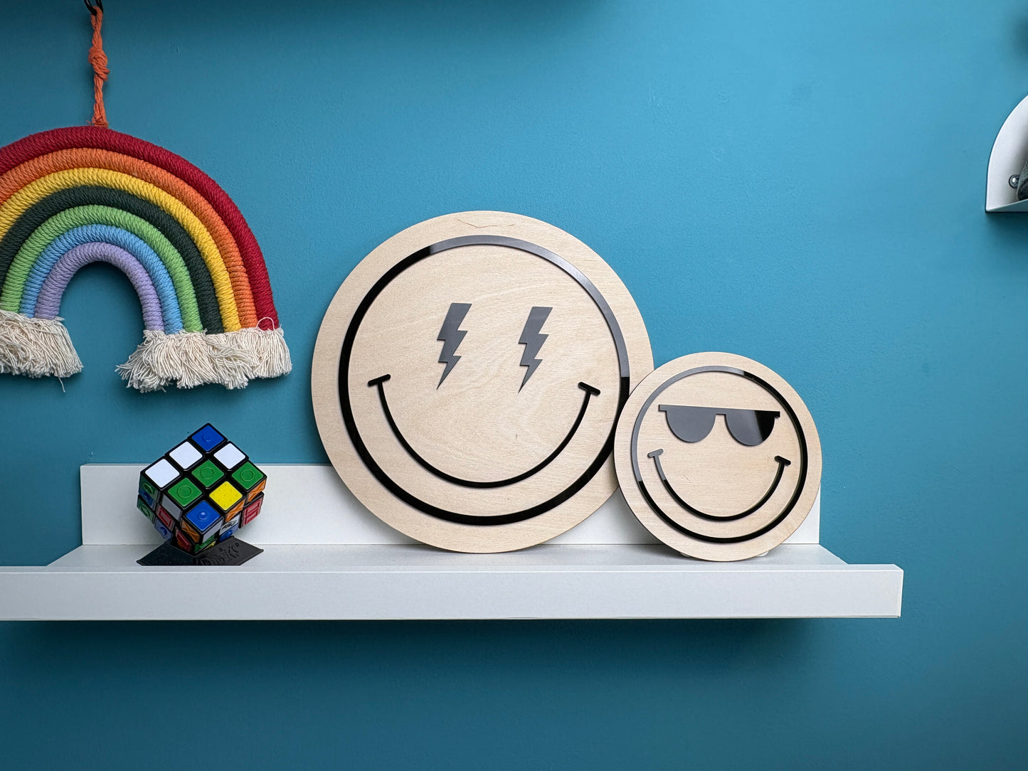 Two round decorative items with smiley face designs on a shelf against a blue wall.