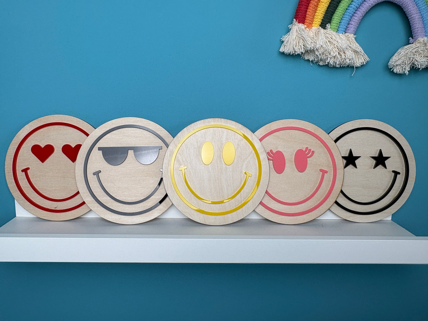 Five wooden emoji coasters on a white surface with a blue background