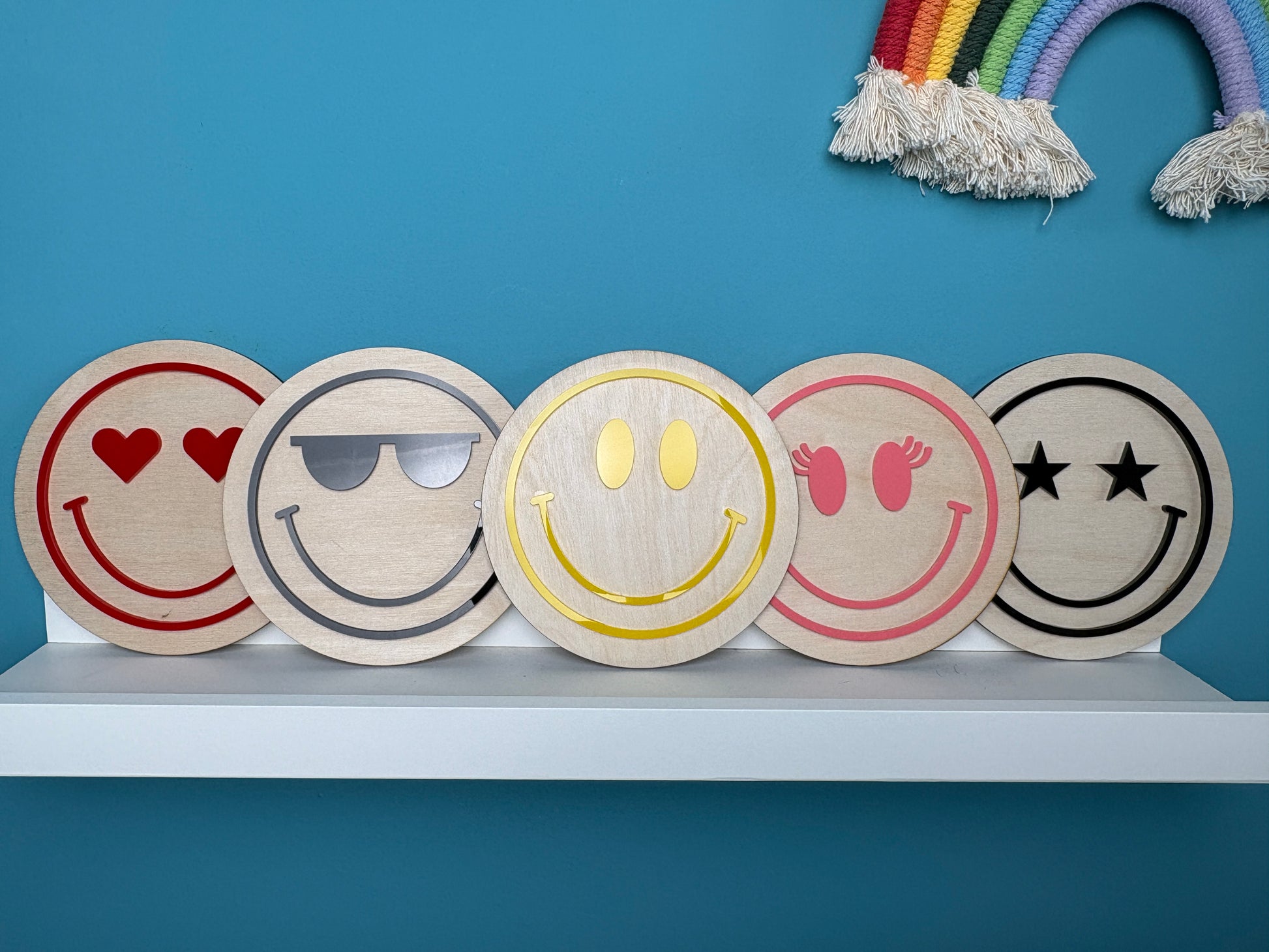 Five wooden emoji coasters on a white surface with a blue background
